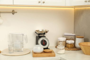Retro mekanik mutfak ölçeği, farklı çatal bıçaklar ve beyaz mermer mutfak tezgahında gıda ürünleri.
