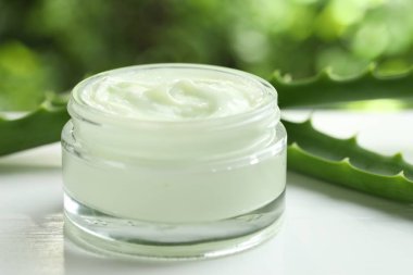 Kavanozda aloe vera özütüyle nemlendirici krem ve beyaz ahşap masa üzerindeki yaprakları bulanık yeşil arka planda, yakın plan