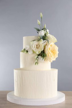 Ahşap masadaki çiçeklerle süslenmiş nefis düğün pastası. Gri arka plan, yakın plan.