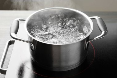 Kaynar suyla pişirme tenceresi ve soba gri arka planda, yakın plan