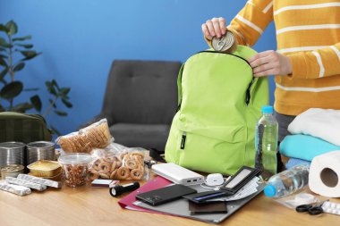 Hayatta kalma kiti. Kadın, ahşap masada sırt çantasına farklı acil durum malzemeleri yerleştiriyor.