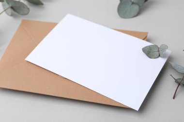 Boş tebrik kartı, kağıt zarf ve okaliptüs yaprakları açık gri arkaplanda, yakın plan