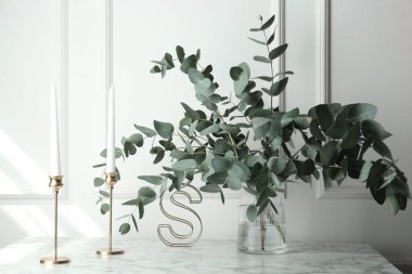 Vazoda yeşil okaliptüs dalları ve beyaz duvarın yanındaki mermer masa üzerindeki diğer dekorlar.