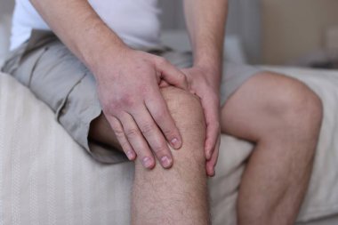 Evdeki yatakta diz ağrısı çeken bir adam, yakın plan.