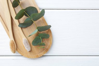 Bambu diş fırçaları ve okaliptüs dalları beyaz ahşap masa, üst manzara. Metin için boşluk