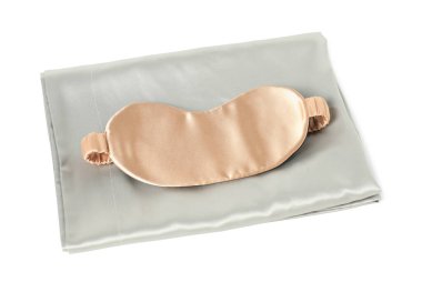 Beyaz arka planda ipek çarşaflar ve uyku maskesi.