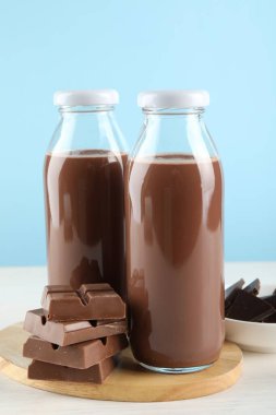 Lezzetli çikolatalı süt ve beyaz masadaki parçalar açık mavi arka plana karşı