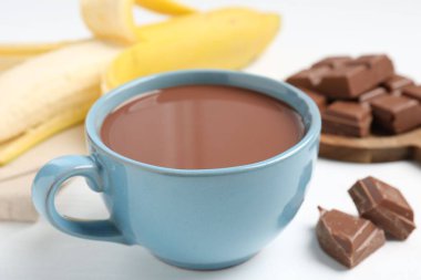 Lezzetli çikolatalı süt, parçalar ve muz beyaz masada, yakın plan.