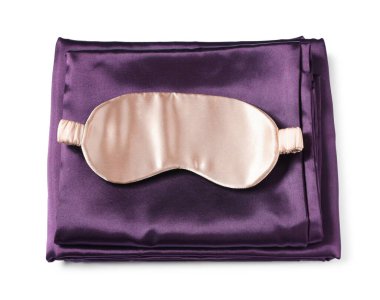 Beyaz arka planda ipek çarşaflar ve uyku maskesi, üst manzara.