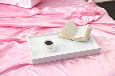 Lüks ipek çarşaflar, kahve tepsisi ve yatakta kitap.