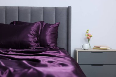 Lüks ipek çarşaflar yatağın üzerinde ve komodinin üzerinde.