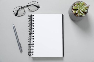 Açık gri zemin üzerinde boş defter, gözlük, kalem ve çiçek dekoru, düz uzanma