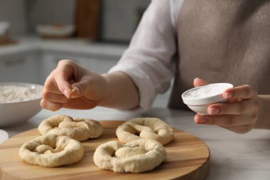 İçerideki masada pişmemiş krakerlere deniz tuzu ekleyen kadın, yakın plan.