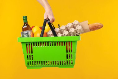 Sarı arka planda farklı ürünleri olan alışveriş sepeti tutan adam, yakın plan.