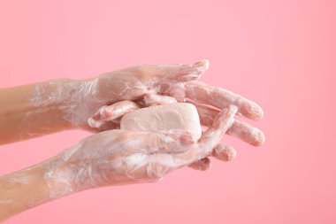 Açık pembe arka planda ellerini sabunla yıkayan kadın, yakın plan.