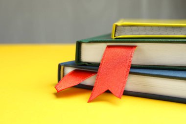 Sarı masadaki kırmızı kurdele yer imlerine sahip kitaplar gri arkaplanda, yakın plan