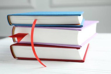 Gri duvara karşı beyaz tahta masada kırmızı kurdele yer imleri olan kitaplar, yakın plan.