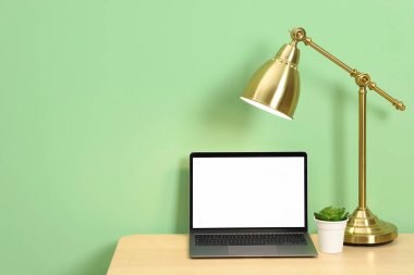 Modern dizüstü bilgisayarı olan, açık yeşil duvarın yanındaki ahşap masada şık bir iş yeri. Metin için boşluk