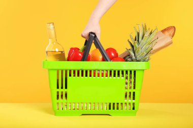 Sarı arka planda ürünlerle dolu alışveriş sepeti olan bir kadın.