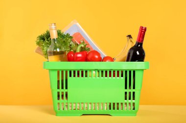 Sarı arka planda farklı gıda ürünleri olan alışveriş sepeti.