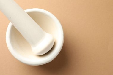 Açık kahverengi arka planda seramik havan ve tokmak, üst manzara. Metin için boşluk