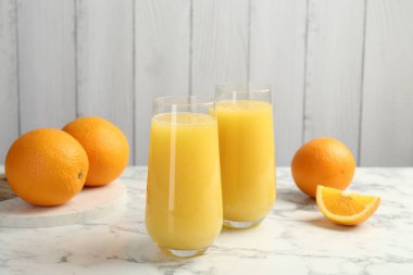 Bardakta portakal suyu ve beyaz mermer masada taze meyve.