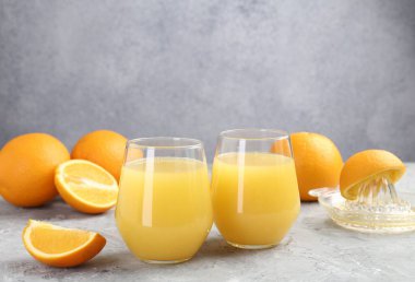 Bardakta portakal suyu, gri masada taze meyve suyu ve meyve sıkacağı.