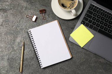 Not defteri, kalem, yapışkan not, kahve, cilt klipsleri, ve gri masada dizüstü bilgisayar, düz konum