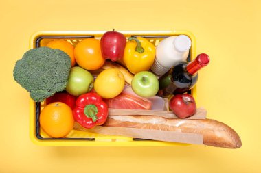 Sarı arka planda ürünlerle dolu plastik alışveriş sepeti.