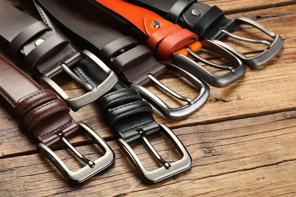 Ahşap masada birçok farklı deri kemer, yakın plan.