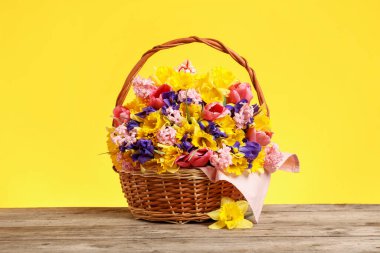 Tahta masanın üzerinde sarı arka planda güzel çiçekler olan sepet.