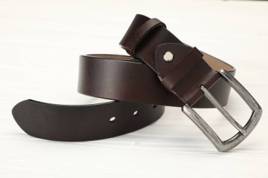 Beyaz ahşap masada kahverengi bir deri kemer, yakın plan.