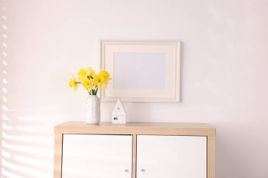 Vazodaki güzel nergisler, şık ev dekorları ve odadaki dolaptaki resim çerçeveleri.