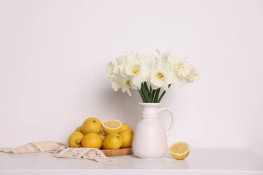 Vazodaki güzel nergisler ve beyaz ahşap masadaki limonlar