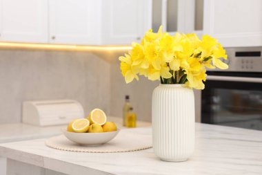 Vazodaki güzel nergisler ve mutfaktaki beyaz mermer masada limonlar.