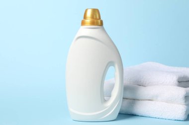 Bir şişe yumuşatıcı ve açık mavi arka planda havlular.