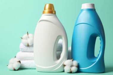 Kumaş yumuşatıcı şişeler, pamuk çiçekleri ve turkuaz arka planda havlular.