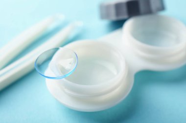 Açık mavi arkaplanda kontak lensler, bavul ve cımbızlar, yakın plan