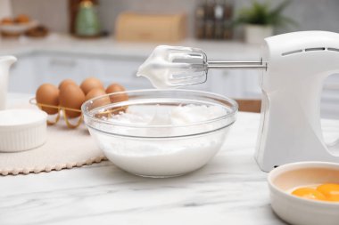 Çırpılmış çırpılmış çırpılmış krema ve yumurta dolu el çırpıcısı, mutfakta beyaz mermer masanın üzerinde.