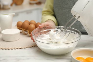 Beyaz mermer masada el çırpıcı kremalı bir kadın, yakın plan.