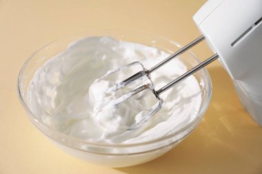 Bej arka planda çırpılmış krema ve çırpılmış kremayla el çırpıcı, yakın plan.