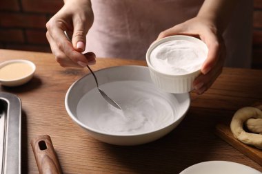 Kraker yapıyorum. Ahşap masada bir kase suya kabartma tozu ekleyen kadın, yakın plan.