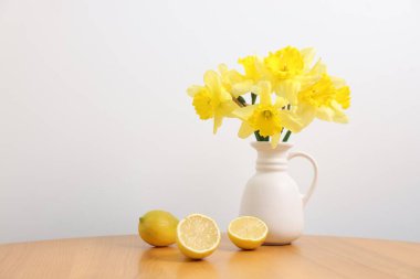 Vazodaki güzel nergisler ve evdeki beyaz duvarın yanındaki ahşap masada limonlar.