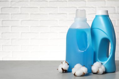 Beyaz tuğla duvara karşı gri masada yumuşatıcı ve pamuk çiçekleri, metin için yer