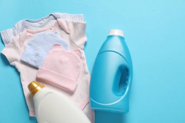 Yumuşatıcı şişeler ve açık mavi arka planda bebek kıyafetleri.