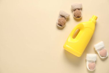 Bir şişe yumuşatıcı ve bej arka planda bebek çorapları. Metin için boşluk