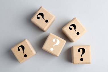 Açık gri arkaplanda soru işaretleri olan tahta küpler, üst görünüm