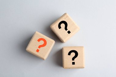 Açık gri arkaplanda soru işaretleri olan tahta küpler, üst görünüm