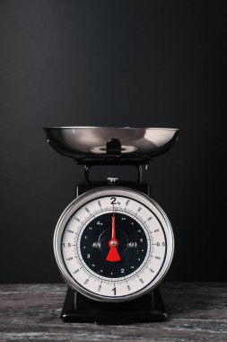 Mekanik mutfak terazisi, siyah arka planda koyu dokulu tabakta.