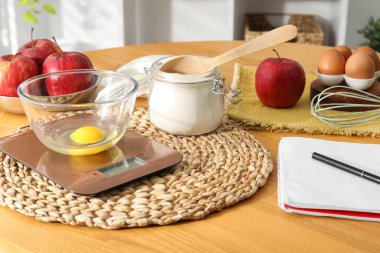 Elektronik mutfak ölçeği, ürünler ve ahşap masa üzerindeki kırtasiye.